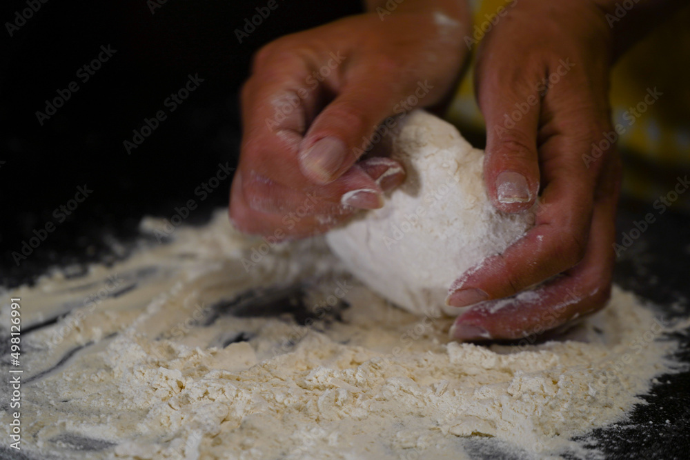 The cooking process of a bread dough. Baking bread recipe. Bakery breads food, detail view with woman hands working on dough at an old wood pan. flour falling on a dark table. detail. The cooking process of a bread dough. Baking bread recipe. Bakery breads food, detail view with woman hands working on dough at an old wood pan. flour falling on a dark table. detail.