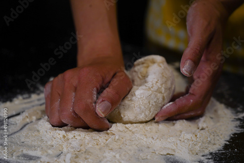 The cooking process of a bread dough. Baking bread recipe. Bakery breads food, detail view with woman hands working on dough at an old wood pan. flour falling on a dark table. detail.