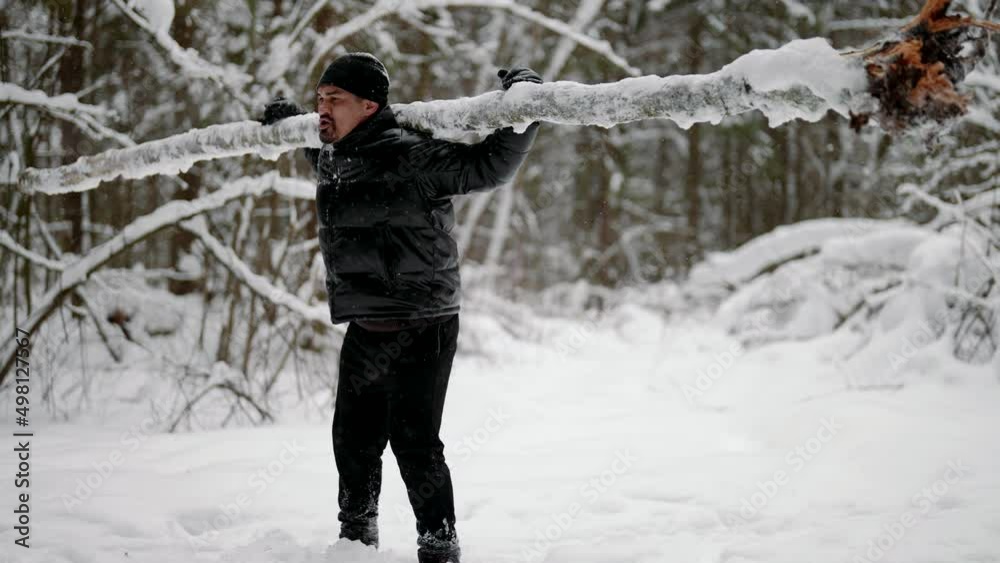 training in nature in winter day, middle-aged man in black clothes is holding log on shoulders training in nature in winter day, middle-aged man in black clothes is holding log on shoulders