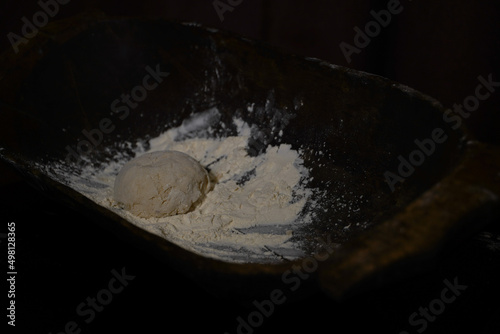 The cooking process of a bread dough. Baking bread recipe. Bakery breads food, detail view with woman hands working on dough at an old wood pan. flour falling on a dark table. detail. © samy