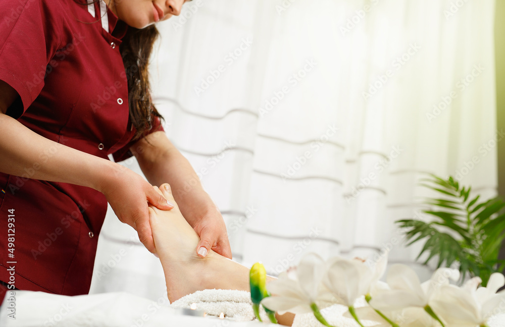 Cropped photo of a masseur spacialist in red uniform making feet massage procedure to a client woman in spa salon. Cropped photo of a masseur spacialist in red uniform making feet massage procedure to a client woman in spa salon.