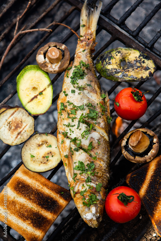 Freshly cooked fish with vegetables and bread in nature. A successful fishing in nature with a grilled fish. Freshly cooked fish with vegetables and bread in nature. A successful fishing in nature with a grilled fish.