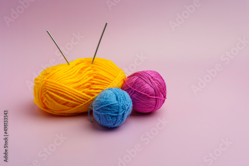Yarn for knitting different colors on a pink background. The spokes are stuck in