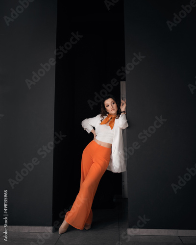 Business young woman standing near a black wall she is wearing a white jacket and orange pants