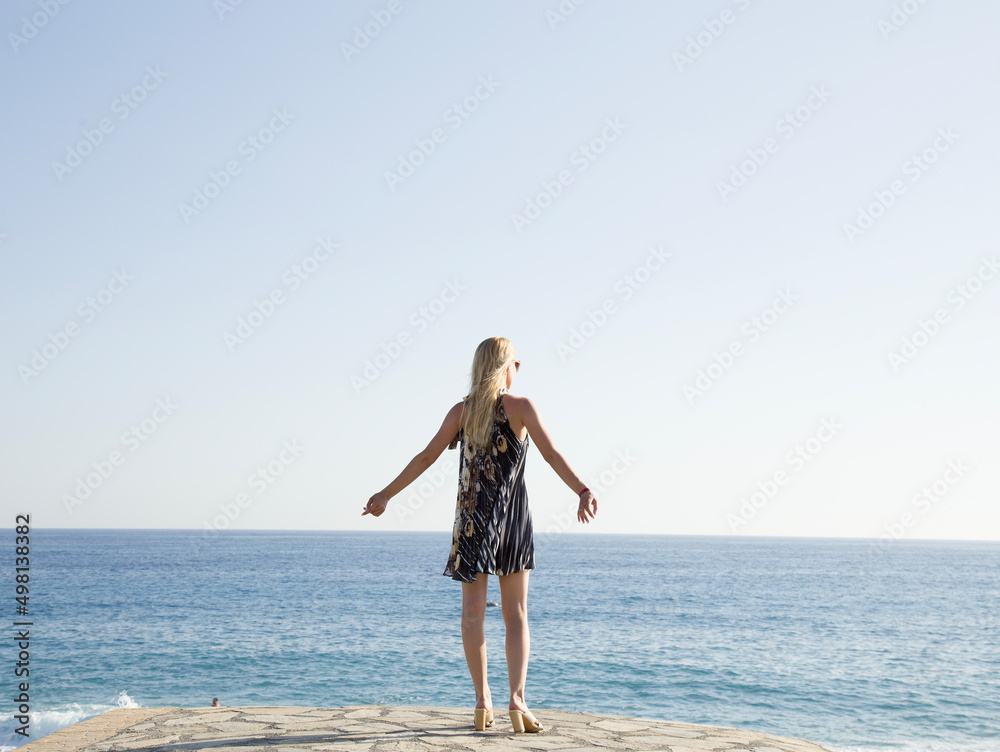 Seascape during sunset. Girl on the beach in the summertime. A young, happy woman walking on the beach with her hands up in a pleated dress Seascape during sunset. Girl on the beach in the summertime. A young, happy woman walking on the beach with her hands up in a pleated dress