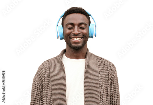 Portrait of happy smiling african man listening to music in wireless headphones wearing brown knitted cardigan isolated on white background