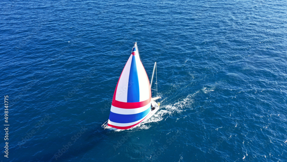Aerial drone photo of beautiful sailboat with colourful sails cruising in the deep blue Aegean sea, Greece