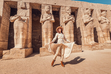 A happy tourist girl in a dress is interested in Egyptology and archaeology and gets a travel experience at the Karnak Temple in Luxor.