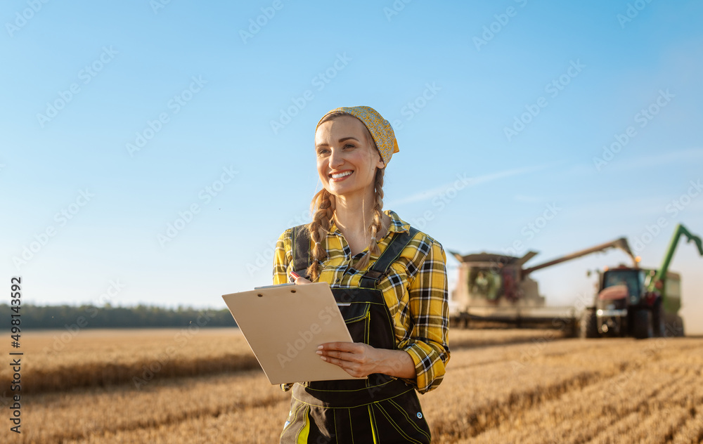 Farmer on grain field with tractor and combine harvester in background taking notes Farmer on grain field with tractor and combine harvester in background taking notes