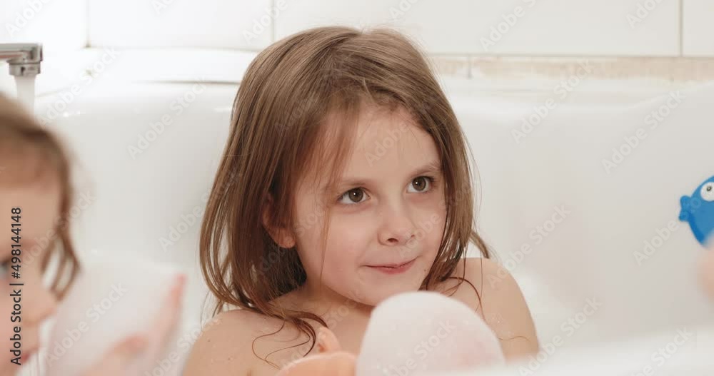 The twin girls are playing in the bathroom with foam and toys. Children's favorite games in the bathroom.