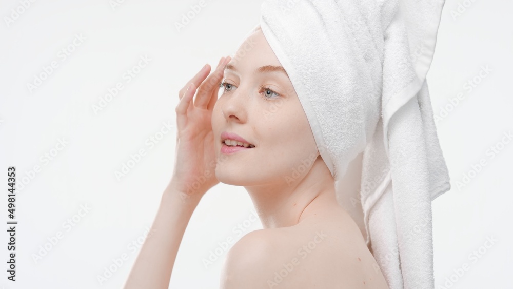 Ginger young Caucasian woman with a towel on her head touches her face turning her head and looking aside on white background | Skin care concept Ginger young Caucasian woman with a towel on her head touches her face turning her head and looking aside on white background | Skin care concept