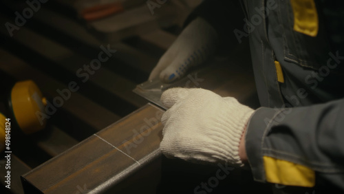 Metalworker in the workshop makes measurements with ruler, calculations and puts serifs with chalk. Locksmith in special clothes and goggles works in production. Slow motion. Close up