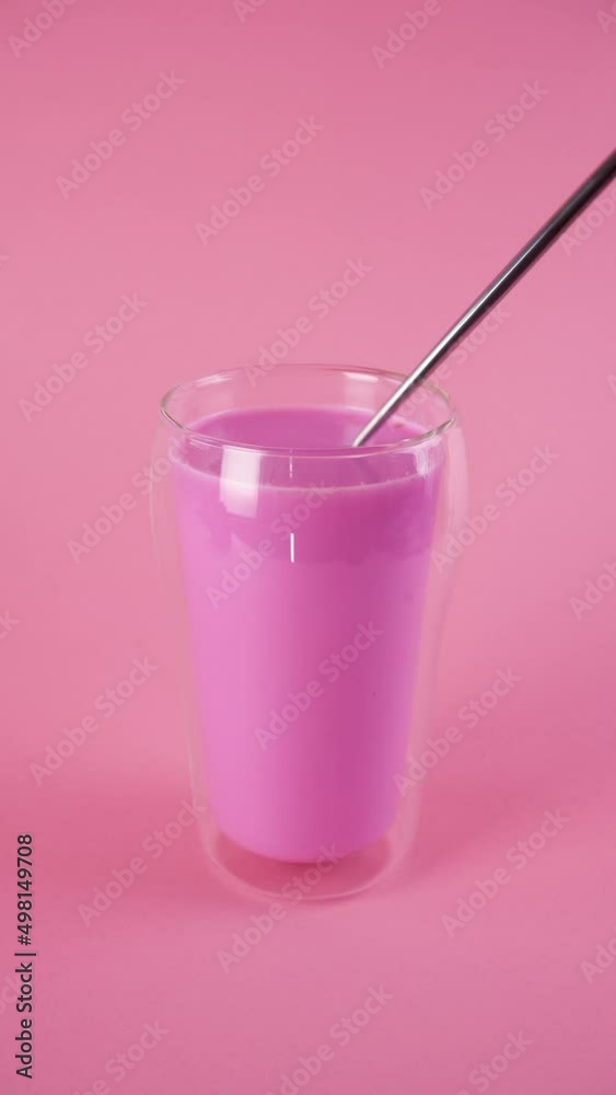 Mixing pink rose milk with a spoon. Glass of moon milk. Vertical orientation. Mixing pink rose milk with a spoon. Glass of moon milk. Vertical orientation.