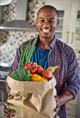 Ive started to eat healthier. Cropped portrait of a handsome young man holding a bag of groceries in the kitchen at home. photo