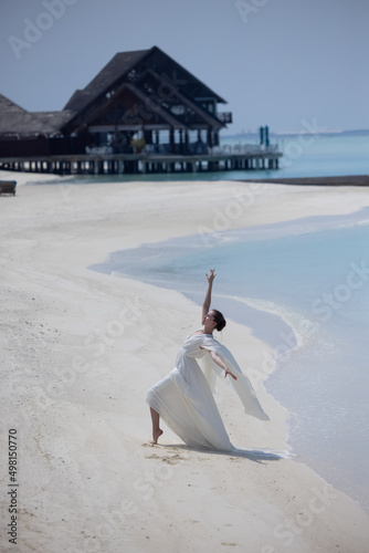 Young girl in white dress dancing on the beach in the Maldives. Bungallow at the background. White sand. photo