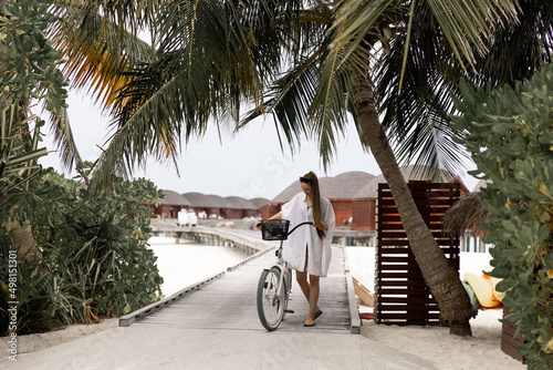 Young girl in white shirt with a bike on the wooden bridge in the Maldives. Bungallow at the background. Island. photo