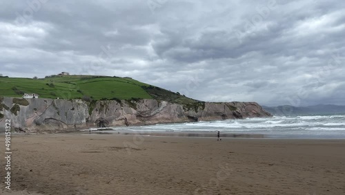 Lonely person walking on Itzurun beach by cliff coast and rough sea on cloudy day in Zumaia. Alone in nature, freedom concepts