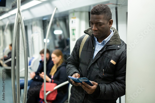 African American man browsing and typing messages on phone on way to work in modern metro car