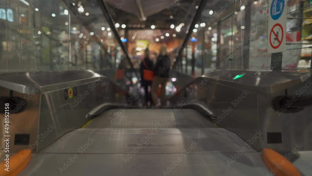 Flat escalator in a supermarket. Elevator and customers with a grocery basket going down the back view, unrecognizable personality. Making the purchase. Shopping lifestyle concept. 