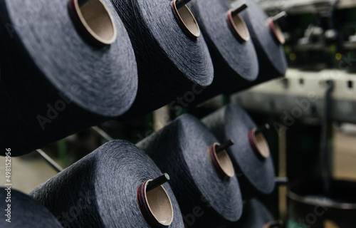 Spools of black cotton thread on a stand near the production line.