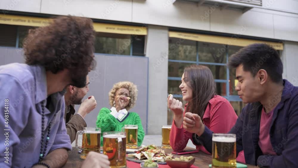 Happy young modern friends enjoying time together eating tapas and drinking beer in outdoors bar celebrating holiday trip Happy young modern friends enjoying time together eating tapas and drinking beer in outdoors bar celebrating holiday trip