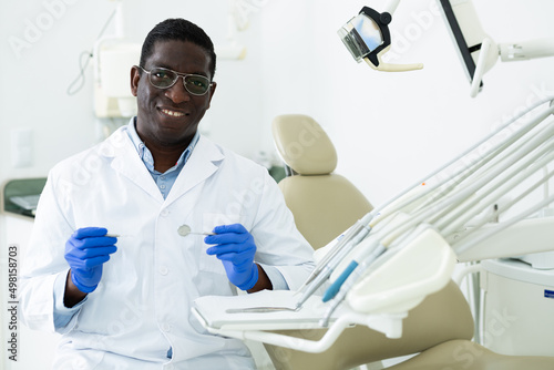 Portrait of successful smiling professional african american dentist standing in white coat in modern medical dental office..