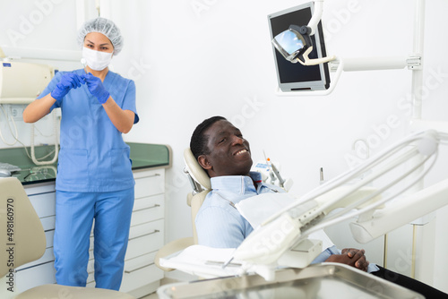 Smiling adult african american man sitting in chair in dental office  satisfied with result of teeth treatment..