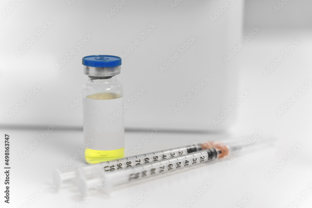 Syringes with needles in caps are lying next to vial with medical solution or vaccine with empty label for template, standing on table, prepared for patient in clinic. Insulin syringes for diabetics Syringes with needles in caps are lying next to vial with medical solution or vaccine with empty label for template, standing on table, prepared for patient in clinic. Insulin syringes for diabetics