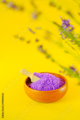 purple sea bath salt in a round wooden cup and blooming lavender on a bright yellow background.body cosmetic with lavender extract.Aromatherapy and spa.lilac salt with lavender extract