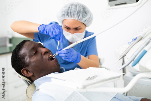 Confident woman stomatologist treating teeth to african american patient in modern dental office..