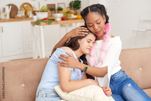 A young black woman comforts and helps her female caucasian friend solve problems.