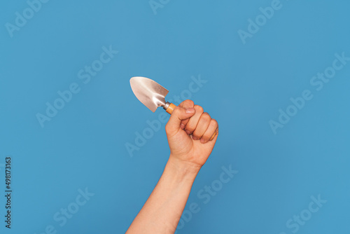 Woman's hand with small shovel against blue background.
