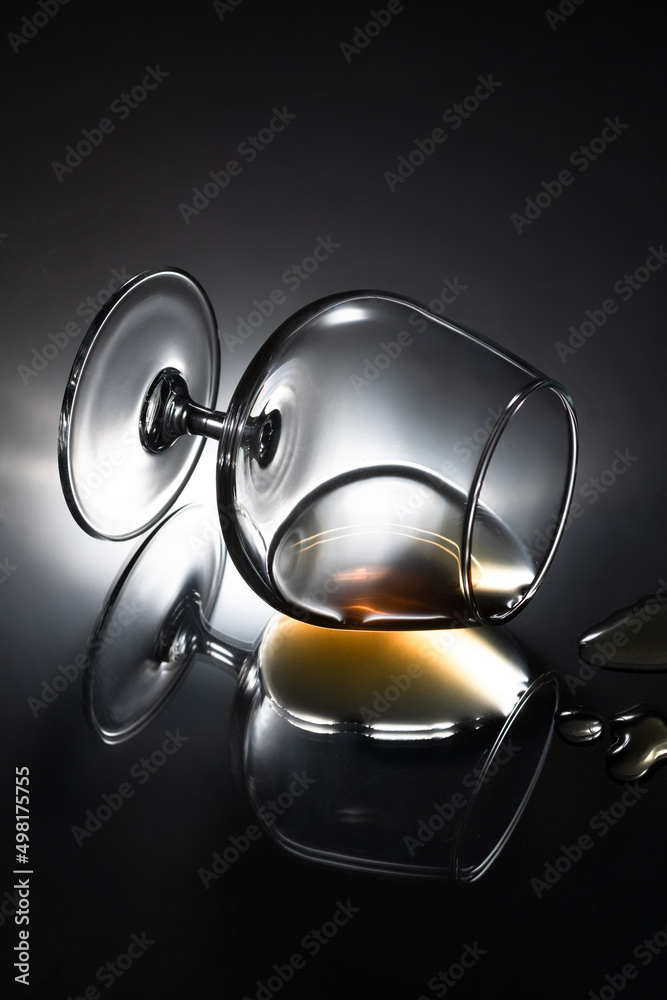Cognac glass with strong alcohol lies on a mirror table with drops of cognac Cognac glass with strong alcohol lies on a mirror table with drops of cognac