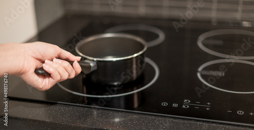 Female hand holding a pot that is put on the electric pan in the kitchen.
