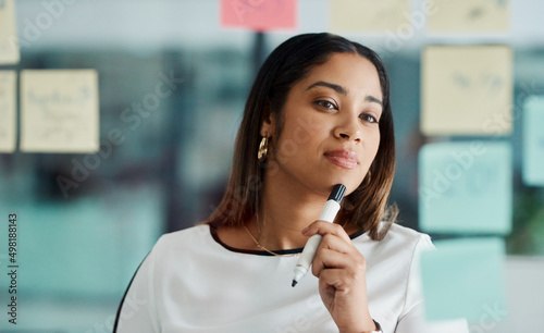 Brainstorming improves your critical thinking and problem-solving skills. Shot of a young businesswoman brainstorming with notes on a glass wall in an office. photo