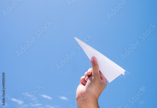 throwing paper plane to the sky, human's hand holding paper craft against blue sky background
