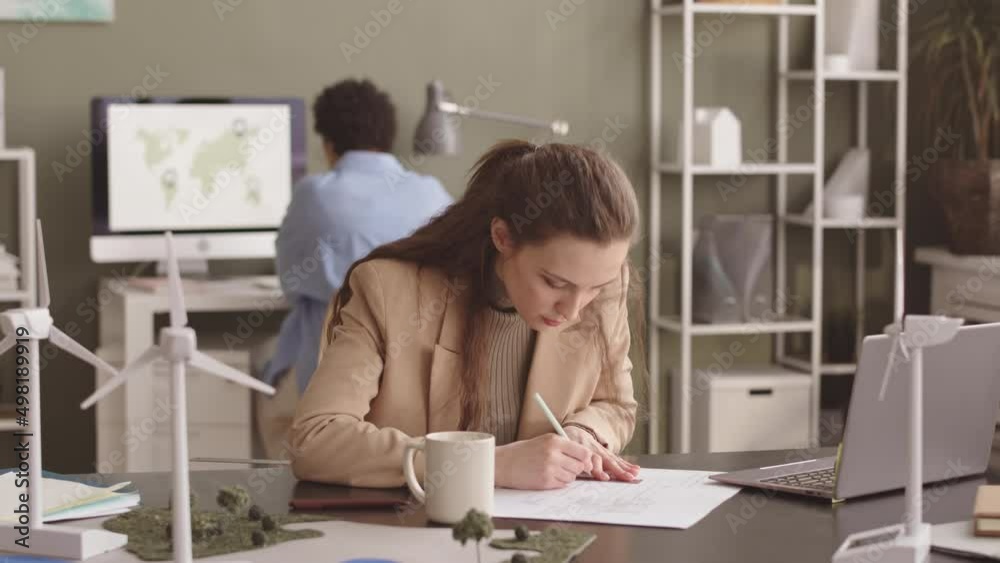 Waist up slowmo of female engineer with ruler and pencil in hands drawing blueprint on paper while creating alternative energy project in office Waist up slowmo of female engineer with ruler and pencil in hands drawing blueprint on paper while creating alternative energy project in office