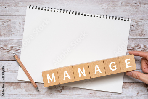 「MANAGE」と書かれた積み木、ノート、ペン、手