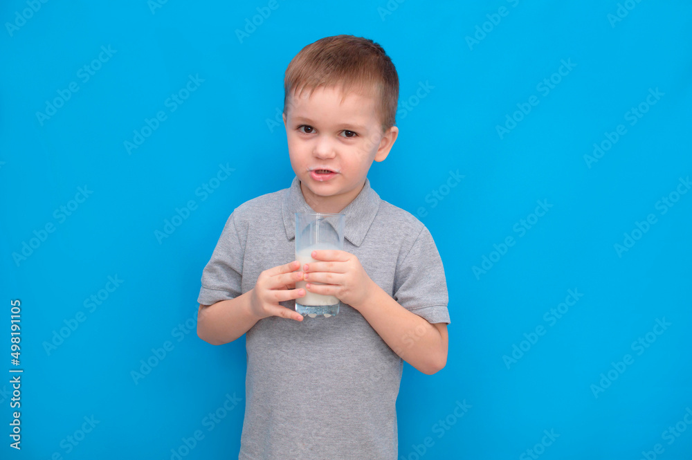 Cute boy 5-6 years old drinking milk on colored blue background. He knows that he needs to drink milk for bone health. The baby loves milk. Concept of children's healthy nutrition Cute boy 5-6 years old drinking milk on colored blue background. He knows that he needs to drink milk for bone health. The baby loves milk. Concept of children's healthy nutrition