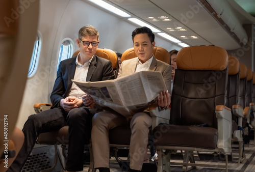 Businessman in brown suit on trip holding business newspaper while reading in plane during flight .