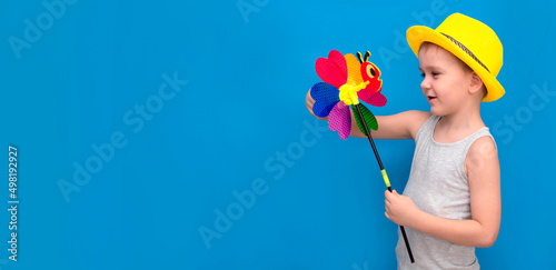child in bright yellow summer hat holds shiny toy breeze standing on a blue background. The boy is enjoying the summer holidays. The concept of a happy childhood. Copy space