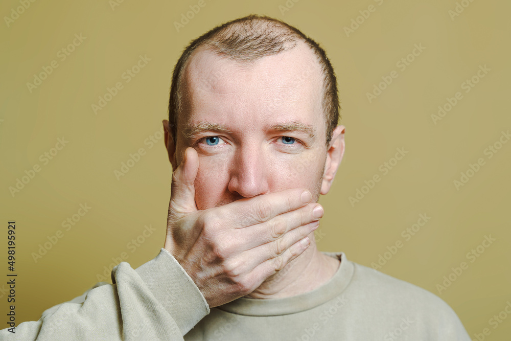 The man covered his mouth with his hand. Portrait of a young man making faces