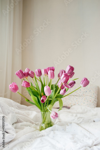 beautiful large bouquet of pink fresh tulips in vase on white linen bed in natural beautiful light. good morning mood. holiday card. cover for printing. selective focus