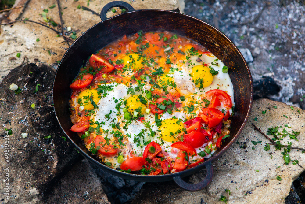 Eggs prepared with vegetables on a frying pan on the fire in the forest. Cooking scrambled eggs over an open fire. Breakfast in nature. Tourist food. Eggs prepared with vegetables on a frying pan on the fire in the forest. Cooking scrambled eggs over an open fire. Breakfast in nature. Tourist food.