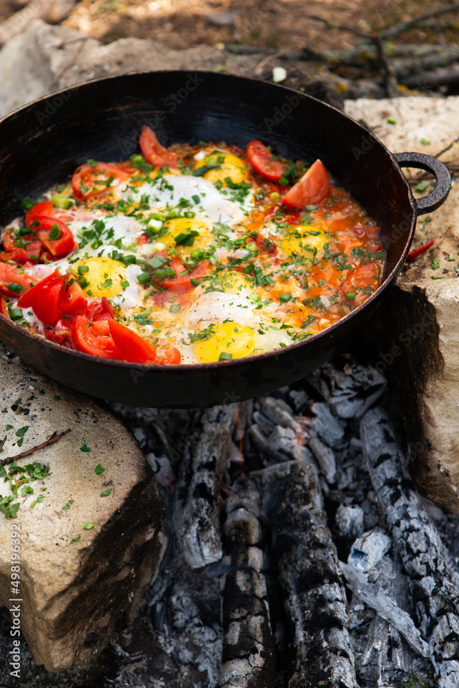 Eggs prepared with vegetables on a frying pan on the fire in the forest. Cooking scrambled eggs over an open fire. Breakfast in nature. Tourist food. Eggs prepared with vegetables on a frying pan on the fire in the forest. Cooking scrambled eggs over an open fire. Breakfast in nature. Tourist food.