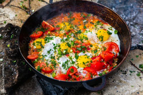 Eggs prepared with vegetables on a frying pan on the fire in the forest. Cooking scrambled eggs over an open fire. Breakfast in nature. Tourist food.