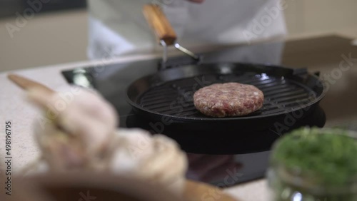 Cooking beefstake patty for burger. Chef roasting fat meat cutlet for hamburger on a metal grill frying pan at restaurant kitchen. American unhealthy fastfood making. photo