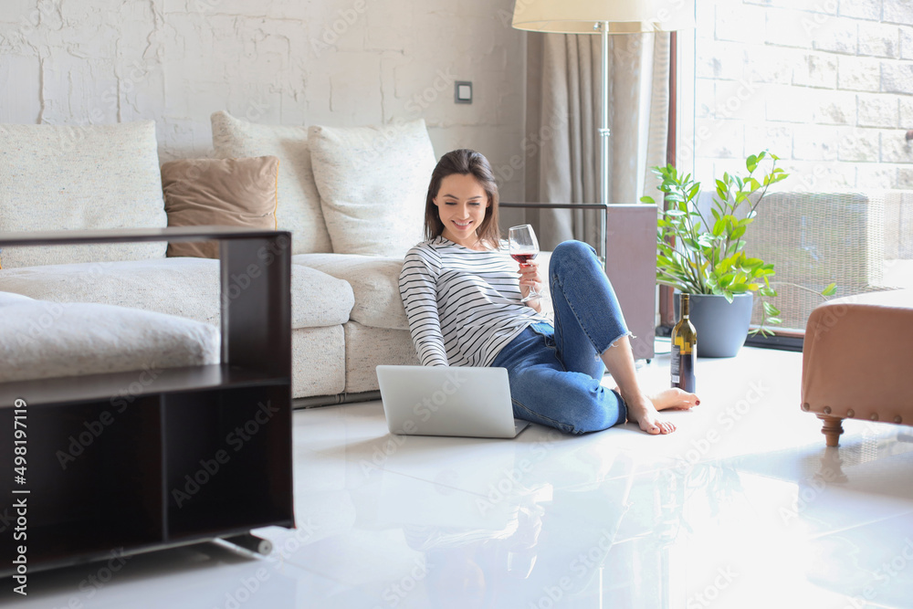 Smiling young woman sitting on floor with laptop computer and chating with friends, drinking wine. Smiling young woman sitting on floor with laptop computer and chating with friends, drinking wine.