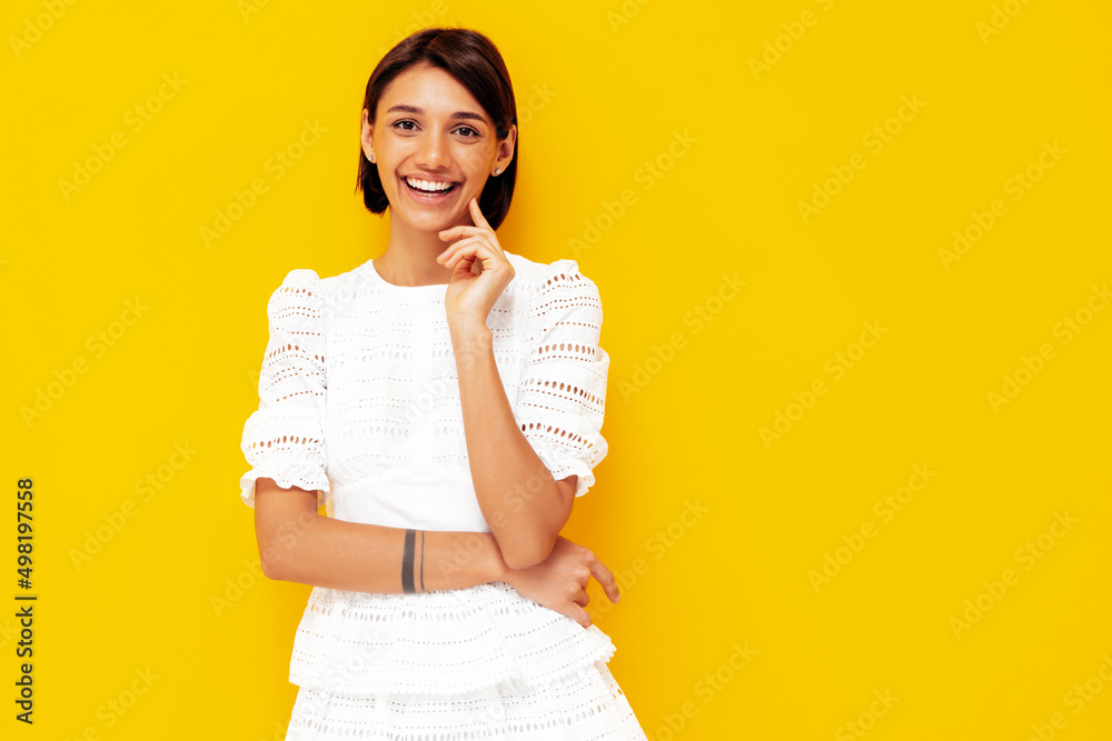 Young beautiful smiling female in trendy summer white dress. Sexy carefree woman posing near yellow wall in studio. Positive model having fun. Cheerful and happy. Isolated Young beautiful smiling female in trendy summer white dress. Sexy carefree woman posing near yellow wall in studio. Positive model having fun. Cheerful and happy. Isolated