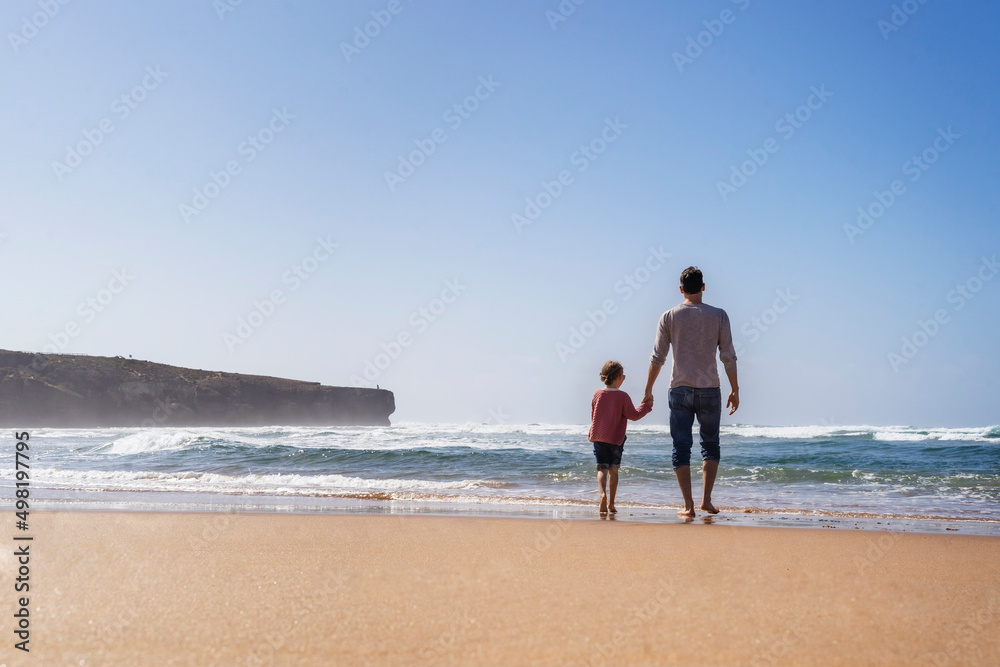Father and daughter walking towards sea on sunny day Father and daughter walking towards sea on sunny day